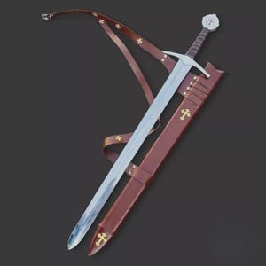 May include: A medieval-style sword with a silver blade and a brown leather scabbard. The hilt features a white pommel with a red cross, and the scabbard has gold cross accents. A brown leather strap is attached.