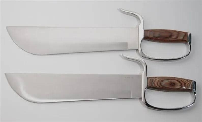 May include: Two large, polished steel blades with curved handles and wooden grips. The handles have a finger loop design. The blades are displayed on a white background.