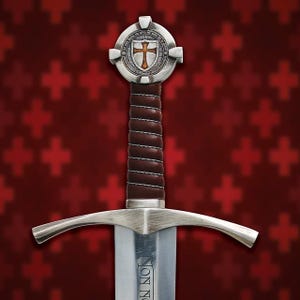 Könnte beinhalten: Ein mittelalterliches Schwert mit silberner Klinge und Parierstange, mit einem braunen, lederumwickelten Griff. Der Knauf hat ein rundes Emblem mit einem Kreuzmuster. Der Hintergrund ist ein Muster aus roten Kreuzen.