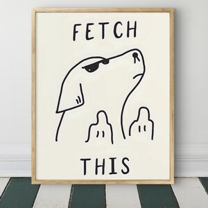 Könnte beinhalten: Ein gerahmter Druck mit einer minimalistischen Hundeillustration. Die schwarze Strichzeichnung zeigt einen Hund mit Sonnenbrille, der nach oben schaut, begleitet vom Text "FETCH THIS" in fetten, schwarzen Buchstaben. Das Kunstwerk ist vor einem cremefarbenen Hintergrund.