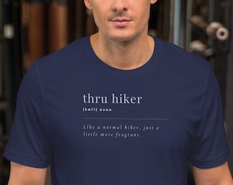 Op de afbeelding: Een marineblauw t-shirt met witte tekst die "thru hiker" luidt en de term definieert als "Net als een normale wandelaar, alleen iets meer geurend."