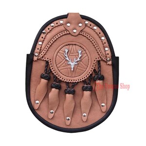 May include: A brown leather sporran with a silver stag head emblem, decorative stitching, and five tassels. The sporran has a black trim and silver studs.