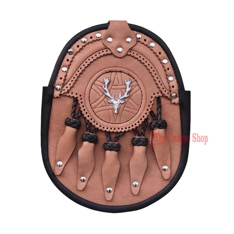 May include: A brown leather sporran with a silver stag head emblem, decorative stitching, and five tassels. The sporran has a black trim and silver studs.