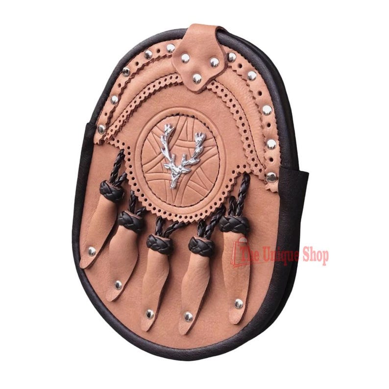 May include: A brown leather sporran with a silver stag head emblem and black braided tassels. The sporran has a decorative design and is adorned with silver studs.