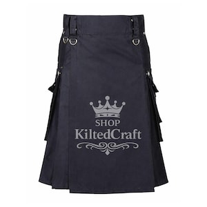May include: A black kilt with silver metal hardware, including D-rings and rivets. The kilt has pleats and pockets. The text "SHOP KiltedCraft" is printed on the front. This traditional garment is suitable for various occasions.