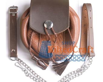 May include: A brown leather sporran with a flap closure and silver-tone hardware. The sporran features a decorative tassel and chain, and a leather strap. The image includes the text "Shop Kilted Craft".