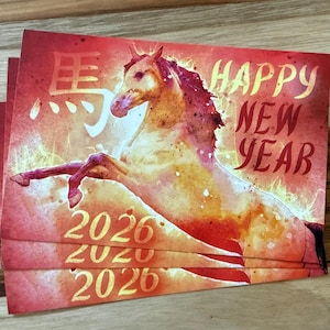 May include: Red and gold Happy New Year cards featuring a watercolor illustration of a horse. The cards have the text "Happy New Year" and the year "2026" in gold lettering. The cards are stacked.