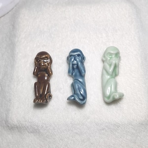 以下が含まれることがあります： 3体のセラミック製の猿の置物。それぞれ茶色、青、緑の色をしています。猿は目、耳、口を隠しており、「悪を見ない、悪を聞かない、悪を言わない」ということわざを表しています。