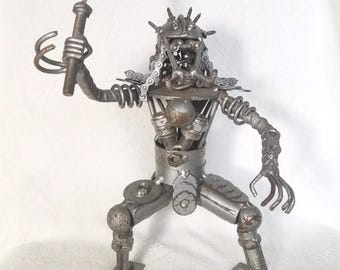 May include: A silver metal sculpture of a creature with a sword, made from recycled metal parts. The creature has a helmet with spikes and a chainmail beard. The sculpture is standing on a white surface.