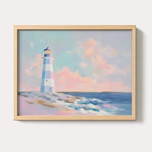 Op de afbeelding: Een ingelijste kunstdruk van een vuurtoren. De vuurtoren is geschilderd met afwisselende witte en pastelblauwe strepen. De lucht is een mix van pastelroze, blauw en geel. De oceaan is diepblauw en de rotsen zijn een mix van wit en grijs.