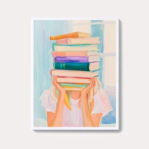 以下が含まれることがあります： カラフルな本を顔の前に積み重ねて持っている人物を描いた芸術的なプリント。本はオレンジ、ピンク、紫、緑など様々な色合いです。人物は白いシャツを着ており、背景は水色と白の配色です。
