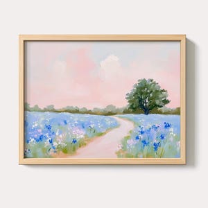 Puede incluir: Pintura de paisaje enmarcada que representa un campo de flores silvestres azules y moradas con un camino sinuoso que conduce a un gran árbol verde. El cielo es de un rosa suave con nubes blancas. El marco es de madera clara.