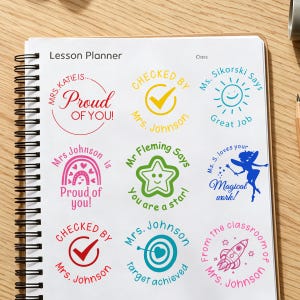 May include: A spiral-bound lesson planner page featuring nine circular teacher stamps in various colors. Designs include text like Mrs. Katie is Proud of You, Checked by Mrs. Johnson, Ms. Sikorski Says Great Job, Mrs. Johnson is Proud of you, Mr. Fleming Says You are a star, Ms. S. loves your Magical work, Checked by Mrs. Johnson, Mrs. Johnson Target achieved, and From the classroom of Mrs. Johnson.
