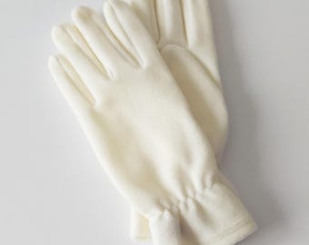 Pode incluir: Um par de luvas de cor creme. As luvas são feitas de um material macio e felpudo. A área do pulso tem um detalhe franzido. As luvas são projetadas para fornecer calor e conforto.