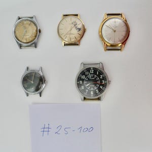 Könnte beinhalten: Fünf Vintage-Armbanduhren mit verschiedenen Designs. Die Uhren haben silber- und goldfarbene Gehäuse mit unterschiedlich farbigen Zifferblättern. Eine Uhr hat ein schwarzes Zifferblatt mit weißen Ziffern. Ein Blatt Papier mit dem Text "# 25-100" befindet sich unten.