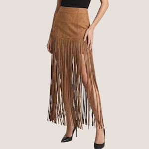 May include: A tan suede-effect midi skirt featuring a high-waisted design and a solid panel at the top. The lower portion of the skirt is composed of long, thin, vertical fringe strips that extend downwards, creating a layered and textured appearance.