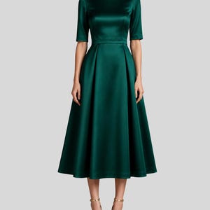 May include: A dark emerald green midi dress with a boat neckline, half-length sleeves, and a fitted bodice that transitions into a pleated, flared skirt. The garment is crafted from a smooth, satin-like fabric with a subtle sheen throughout.