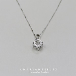 May include: A silver necklace with a cubic zirconia pendant in a square cage setting.