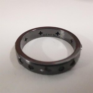 May include: A dark grey ring featuring small circular cutouts and star-shaped designs. The band has the text "ALE MET 54". The ring is a band style and is likely made of metal. The ring is a band style.
