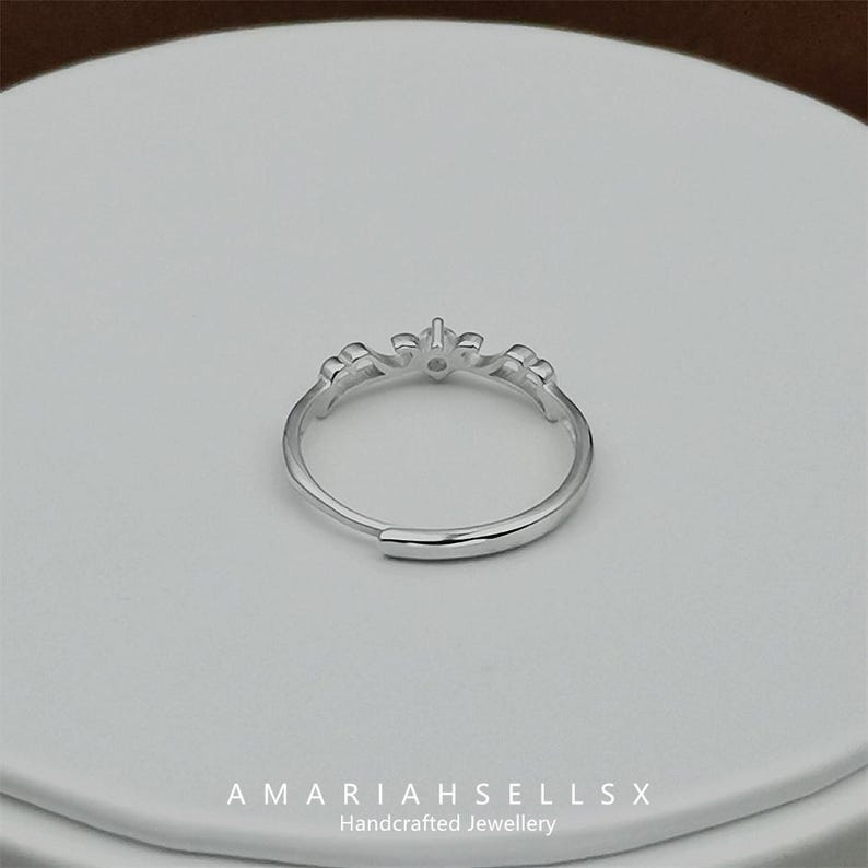 May include: A silver ring with a delicate design featuring a small, clear stone in the centre. The ring is open and adjustable.