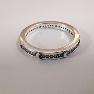 May include: A silver ring featuring a band of small, clear stones. The ring has a repeating pattern of small stars and dots around the top edge. Two crescent moon shapes are on the sides of the ring.