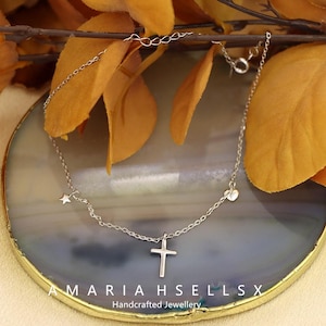 Peut inclure: Un collier en argent avec un pendentif en forme de croix, une étoile et un cœur. Le collier est présenté sur une surface en pierre décorative. Le texte "AMARIAHSELLSX Handcrafted Jewellery" est visible.