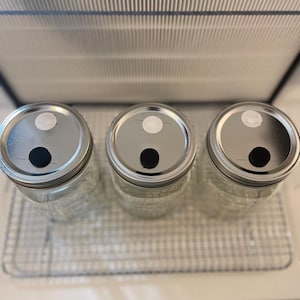 May include: Three clear glass jars with silver lids. Each lid has a white circle with a black dot in the center.