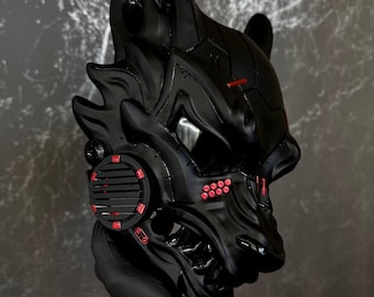 May include: A black, stylized mask with red accents. The mask has a detailed, angular design with a wolf-like appearance. Red details are present on the ears, cheeks, and a circular element on the side. The mask is held by a gloved hand.