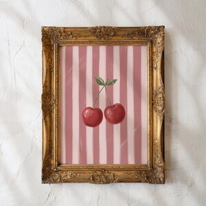 May include: A framed art print featuring two red cherries with green leaves against a pink and white striped background. The ornate gold frame adds a vintage touch to the artwork, suitable for kitchen or dining room decor.