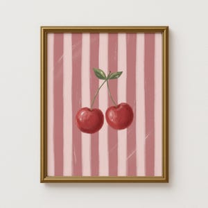 May include: Framed art print featuring two red cherries with green leaves against a pink and white striped background. The artwork is in a gold frame, suitable for kitchen or dining room decor.
