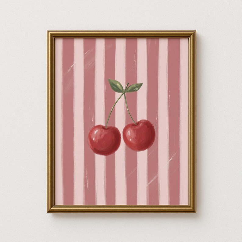 May include: Framed art print featuring two red cherries with green leaves against a pink and white striped background. The artwork is in a gold frame, suitable for kitchen or dining room decor.