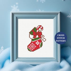 Peut inclure: Un motif de point de croix encadré représentant une chaussette de Noël. La chaussette est rouge avec un motif de flocon de neige blanc et contient une canne en bonbon et des cadeaux emballés. Le cadre est bleu clair, et le texte "CROSS STITCH PATTERN" est sur un cercle bleu.