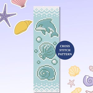 Op de afbeelding: Een kruissteekpatroon met een dolfijn, bellen en schelpen in blauw en wit. Het ontwerp bevat een dolfijn die uit het water springt, een zeeschelp en de tekst "CROSS STITCH PATTERN" in een marineblauwe cirkel.