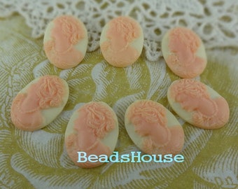 May include: Seven oval-shaped, cream-colored cameo pendants with pink raised images of women's faces. The cameos are arranged in a semi-circle on a white lace background.