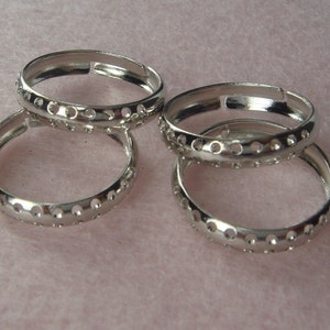 Puede incluir: Cuatro anillos de plata con un patrón decorativo de pequeños agujeros alrededor de la banda. Los anillos están apilados uno encima del otro.
