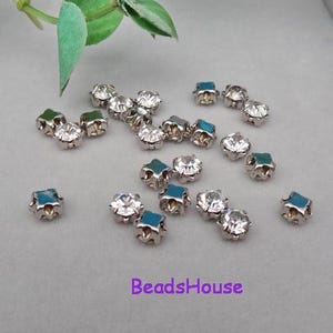 Puede incluir: Una dispersión de piedras de imitación en forma de estrella plateadas con cristales transparentes. Las piedras de imitación tienen un respaldo turquesa.