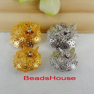 Puede incluir: Dos juegos de adornos metálicos decorativos con diseño de mariposa. Un juego es dorado con una pedrería transparente, el otro es plateado con una pedrería transparente.