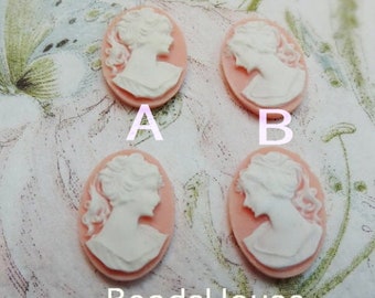 May include: Four oval-shaped cameo pendants with a white cameo image of a woman's profile on a pink background. The cameos are labeled A and B.