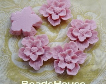 May include: Five pink resin flower cabochons with a raised center and a textured surface. The flowers are arranged in a circle on a patterned fabric background.