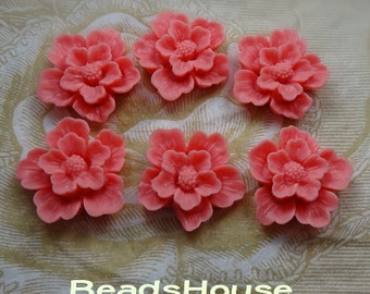 May include: Six coral pink resin flower cabochons with a raised design. The flowers have five petals and a center with a raised circle.