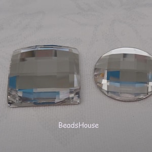 Puede incluir: Dos piedras de cristal transparente, una cuadrada y otra redonda, con un diseño facetado. Las piedras están sobre una superficie blanca.