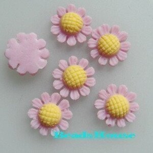 Op de afbeelding: Zes roze en gele suikerdecoraties in de vorm van madeliefjes voor taarten of cupcakes.