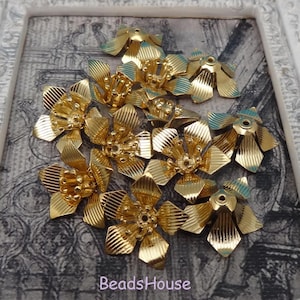 May include: A group of 10 gold metal flower-shaped embellishments with a textured surface. The embellishments are arranged in a random pattern.