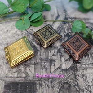May include: Three decorative metal square boxes in gold, bronze, and copper tones. Each box features an ornate, embossed design with a central square and decorative borders. The boxes are hinged and appear to be small containers or jewelry boxes.