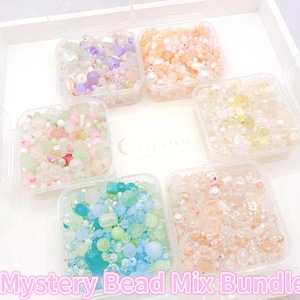 May include: Six clear plastic containers filled with colorful beads, arranged on a white tray. The beads are in various colors, including pink, purple, blue, and green. Text on the image reads "Mystery Bead Mix Bundle 6 x 50g Pack."