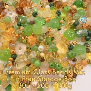May include: A collection of premium glass beads in a variety of shapes and sizes, in shades of green, yellow, and brown. The image includes text that reads "Premium Glass Beads Mix In Free Storage Box 30g 50g 100g."
