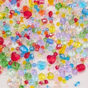 May include: A colourful collection of beads in diverse shapes and sizes. The beads include heart-shaped, round, and faceted designs in shades of red, blue, yellow, green, and purple. These beads are suitable for jewellery making and craft projects.