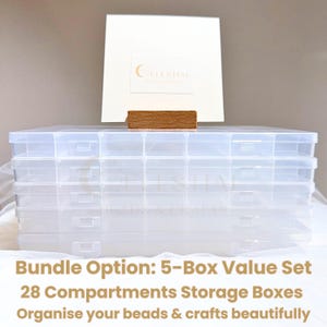 Peut inclure: Ensemble de cinq bo&icirc;tes de rangement en plastique transparent avec plusieurs compartiments. L'ensemble est pr&eacute;sent&eacute; comme un lot de 5 bo&icirc;tes avec 28 compartiments, pour organiser perles et travaux manuels. Une carte blanche et un bloc de bois sont derri&egrave;re.