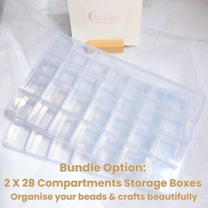 Peut inclure: Deux bo&icirc;tes de rangement en plastique transparent, chacune avec 28 compartiments, id&eacute;ales pour organiser les perles et les travaux manuels. Les bo&icirc;tes sont empil&eacute;es, avec une carte blanche et un support en bois en arri&egrave;re-plan. Le texte sur la carte indique "CELESTIAL".