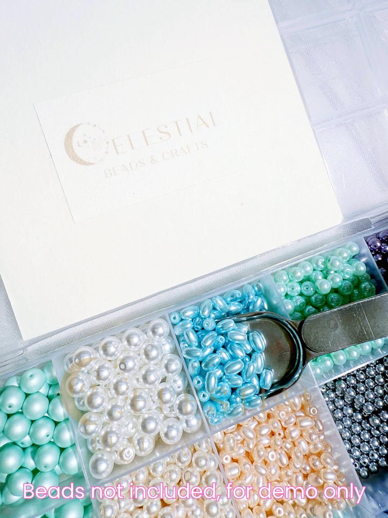 Peut inclure: Un organisateur en plastique transparent rempli de diverses perles color&eacute;es. Les perles sont dans des tons de blanc, de bleu, de vert et de p&ecirc;che. Une paire de ciseaux argent&eacute;s repose dans l'organisateur. Le texte "CELESTIAL BEADS & CRAFTS" est visible.